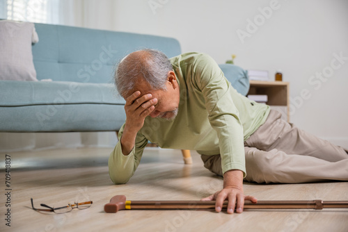 Older senior man headache lying on the floor after falling down he pain and hurt from osteoporosis, Elderly man falling on the floor alone with walking stick at home, Health care and medicine photo