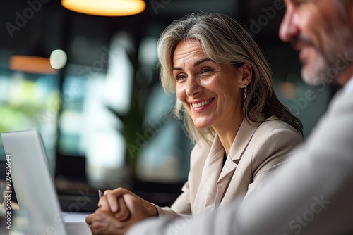 Smiling middle aged professional business woman executive working looking at laptop computer discussing digital data with male colleague at office meeting planning corporate strategy. Generative AI 