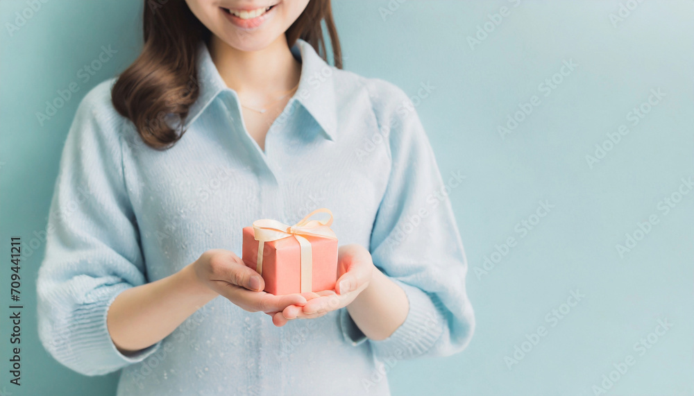リボンがかかった赤い小さなプレゼントの箱を、胸の前に差し出す若い女性の上半身のAI画像 リボンがかかった赤い小さなプレゼントの箱を、胸の前に差し出す若い女性の上半身のAI画像
