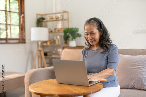 Senior asian woman sitting on sofa using laptop computer, working, chatting, social media internet at home.