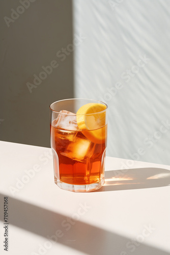 A Glass of Iced Tea with Lemon on White Counter. Artistic Corner Composition. White Background. Bright Lighting and Long Shadow. Minimalist Photo. Minimal Modern Interior. Summer Beverage.