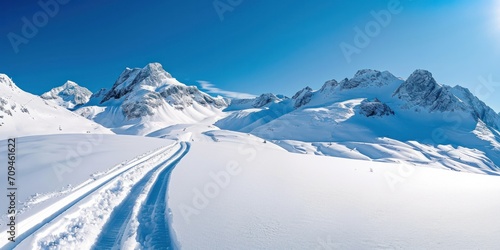 A snowy mountain range with ski tracks, glistening snow, and a clear blue sky