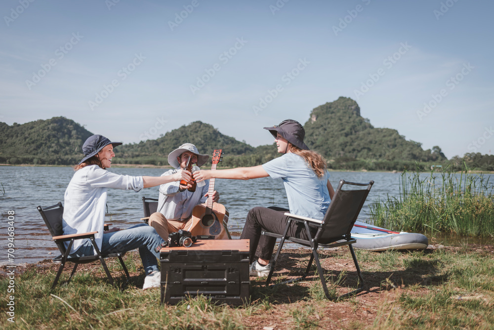 Group of travallers camping with friends they join drinking and playing guitar together with happiness activity camping near nature lake with mountain background is holiday summer camping concept.