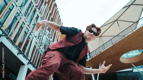 Low angle of asian attractive hipster pose at camera surround by mall. Portrait of break dance choreographer looking at camera while dancing in hip hop style. Outdoor sport 2024. Endeavor.