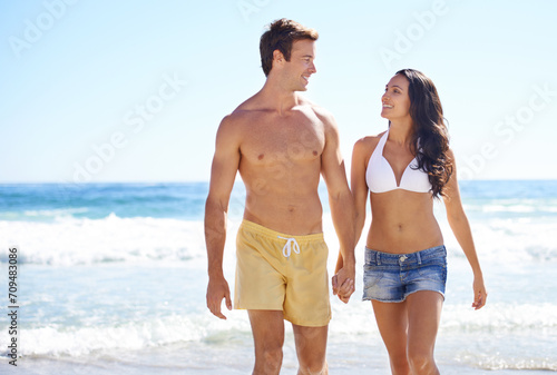 Holding hands, walking and happy couple on beach for holiday adventure together on tropical island with waves. Love, man and woman on ocean vacation with waves, romance and smile on travel in Hawaii.