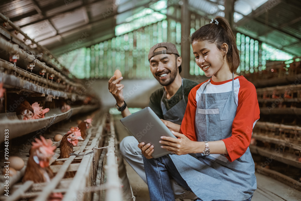 male worker holds an egg while female worker using a shared tablet at a chicken farm