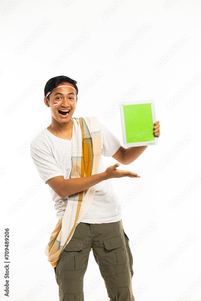 a young asian man in white t shirt and sarong as his shoulder belt standing showing the tablet at his hand and smiling a young asian man in white t shirt and sarong as his shoulder belt standing showing the tablet at his hand and smiling