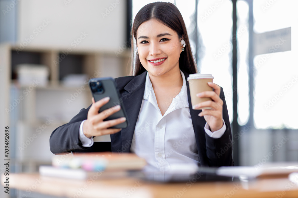 Business Asian woman hold phone and use laptop at the workplace. Project stats financial data sales charts on laptop and cellphone Asian finance concept
