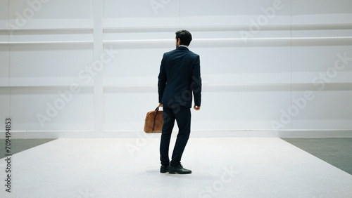 Professional business man standing with cool pose at white background. Manager holding bag while finding partner or looking around. Caucasian working man prepare himself for presentation. Exultant.