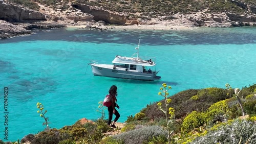 4k Shot of a Young Tourist Exploring the Rugged Landscape of Comino Island, Malta; Views of the Crystal Clear Turquoise Waters of the Blue Lagoon, with a Peacefully Drifting Boat in the Background. photo