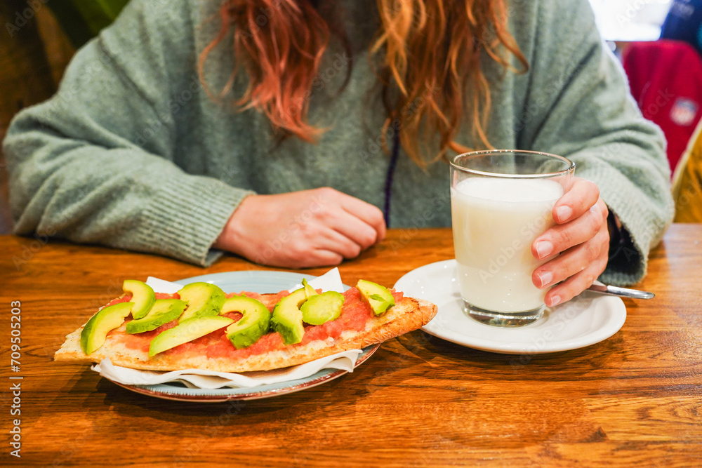 Woman enjoying a healthy snack with milk and avocado toast.