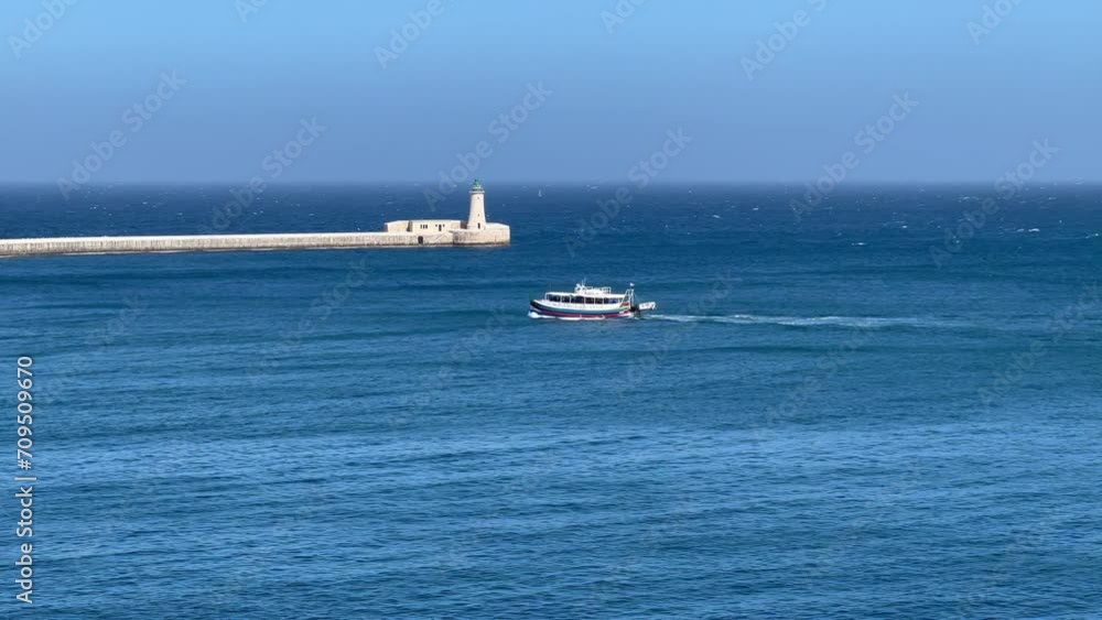 Passenger Ferry Glides Past the Majestic St. Elmo's Lighthouse in 4K, Showcasing the Architectural Grandeur and Historic Significance near Valetta, Malta; Stunning Views of Turquoise Waters. Passenger Ferry Glides Past the Majestic St. Elmo's Lighthouse in 4K, Showcasing the Architectural Grandeur and Historic Significance near Valetta, Malta; Stunning Views of Turquoise Waters.