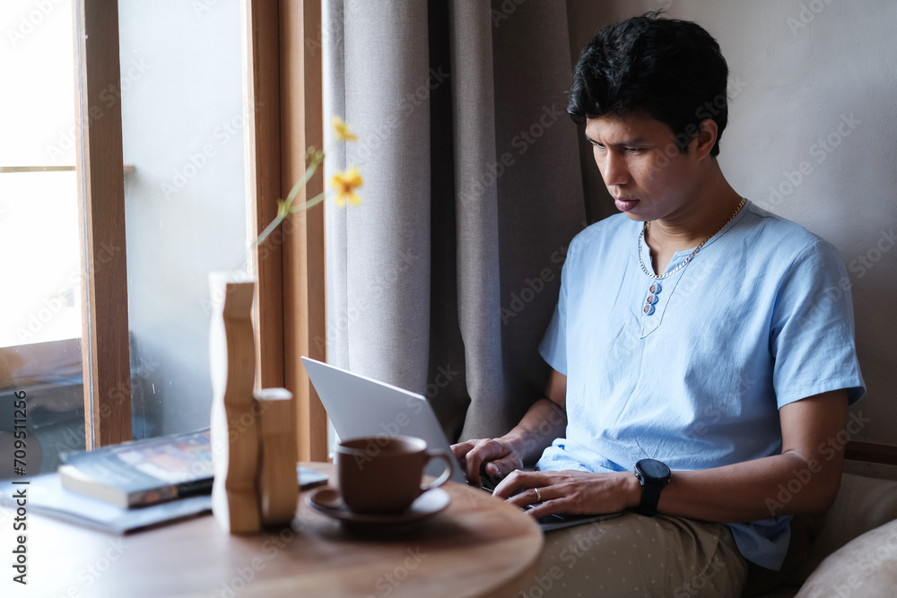 Asian man wearing casual outfit looking serious while checking mail, news, social networks, working on notebook, writing blog, studying at home, resort, hotel on weekend. Online freelance concept. Asian man wearing casual outfit looking serious while checking mail, news, social networks, working on notebook, writing blog, studying at home, resort, hotel on weekend. Online freelance concept.