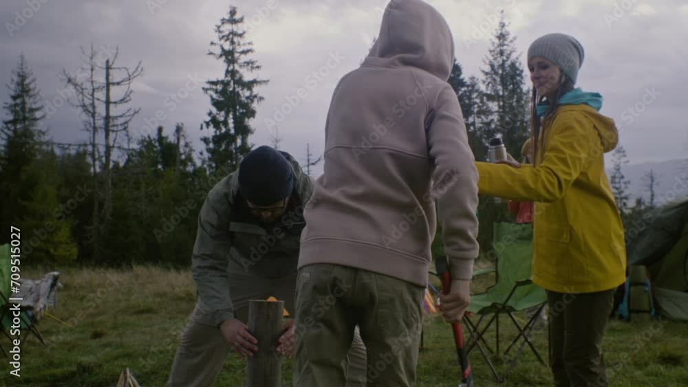 Two tourists chop wood to make fire at camping. Group of multi ethnic travelers stop to rest after long expedition. Outdoor enthusiasts on vacation in forest. Active leisure and tourism. Slow motion. Two tourists chop wood to make fire at camping. Group of multi ethnic travelers stop to rest after long expedition. Outdoor enthusiasts on vacation in forest. Active leisure and tourism. Slow motion.