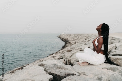 Woman with braids sittingon the rocks at the beach meditating photo