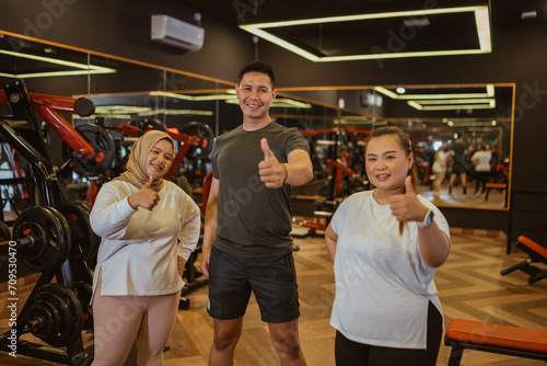 gym instructor and trainee standing with thumb up gesture in gymnasium