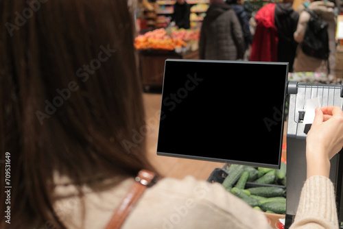 Back view of brown haired Woman customer scanning product in automated self-service checkout terminal in supermarket