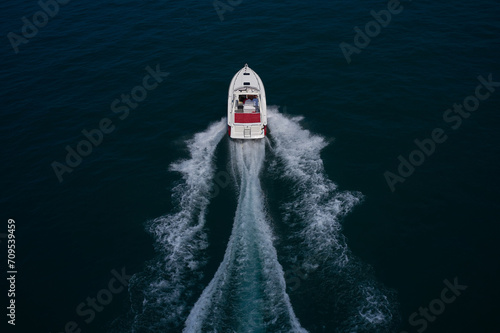 A large red and white boat moves quickly on blue water, rear view from above. A large boat with people moving on the water, aerial view. © Berg