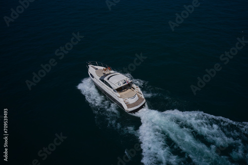 A large white yacht moves on blue water, top view. Men and women on a large white yacht sunbathing, aerial view. Men and women on a white yacht. © Berg