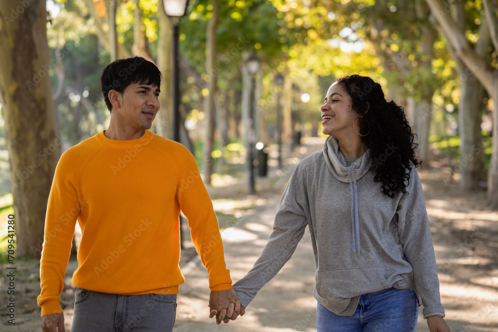 Happy young latin couple holding hands at park and looking at each other.