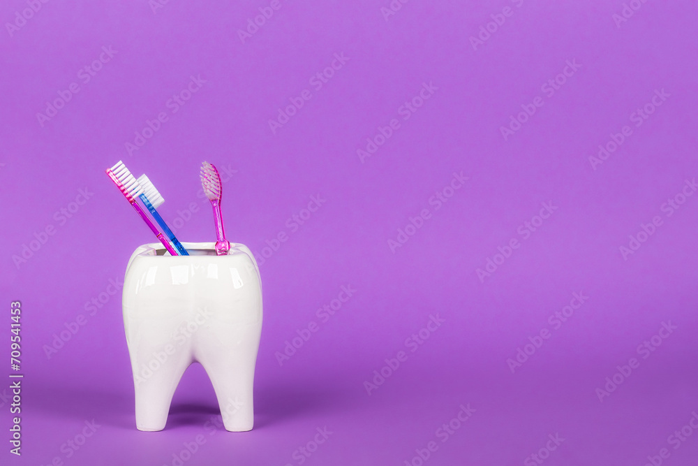 White ceramic tooth bath mug with three toothbrushes in bright colorful background. Free space for text.