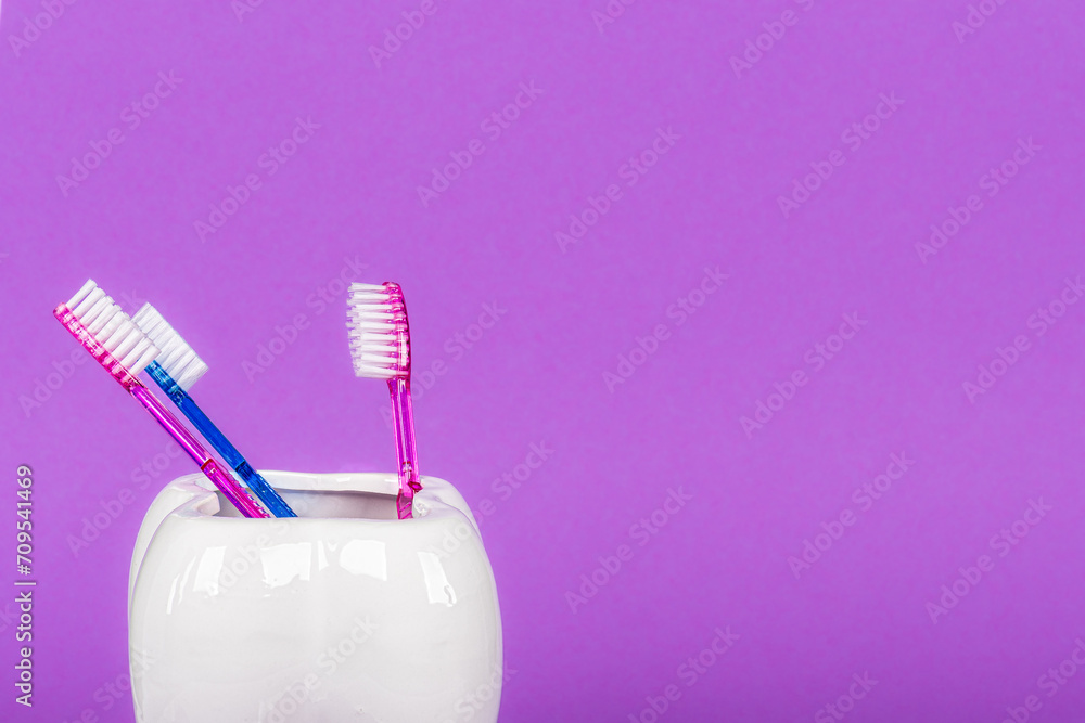 White ceramic tooth bath mug with three toothbrushes in bright colorful background. Free space for text.