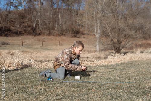 Boy putting work on fishing rod near pond © Cavan