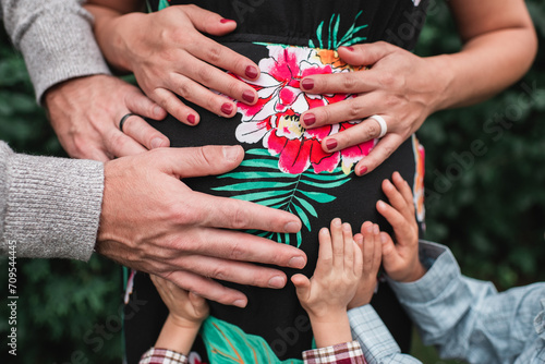 Children's hands and parents' hands holding mother's pregnant belly photo
