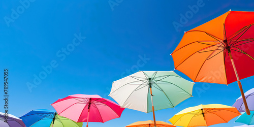 Abstract summer background with colorful umbrellas against blue sky