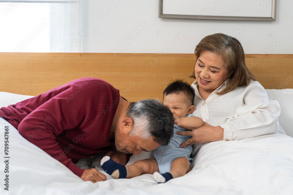 Obraz premium Portrait of happy love asian grandfather with grandmother playing with asian baby on bed, senior, insurance.Big family love with their laughing grandparents smiling together.Family and togetherness
