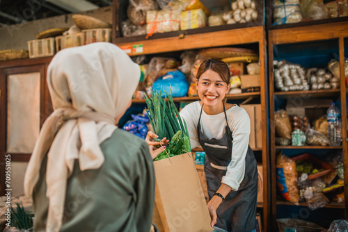 female asian greengrocery seller giving her customer fresh vegetables in paperbag