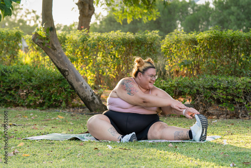 Portrait of the plump woman sitting on the grass doing stretching