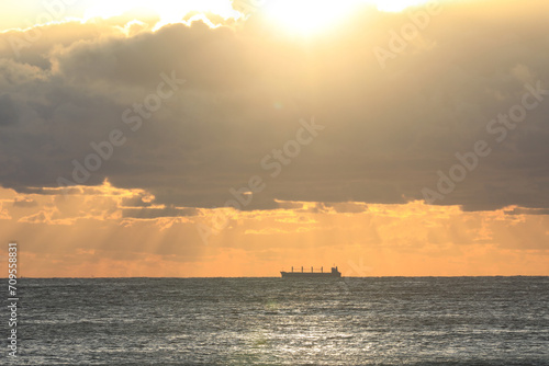 commercial cargo ship sailing in the sun and dark clouds