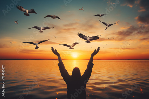 Silhouette of a woman's hands with a flock of pigeons on the background of the lake at sunset © Graphicsstudio 5