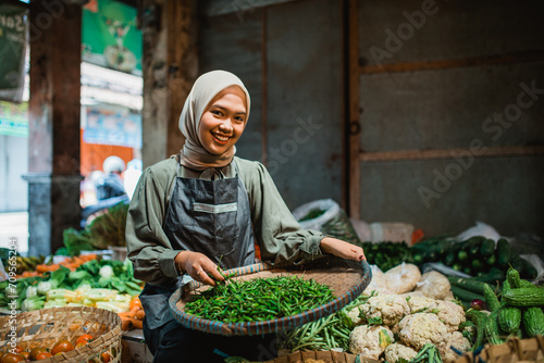 Принти на полотні female asian seller checking greens at vegetable stall in farmer market