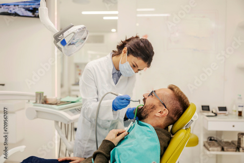 Dentist is drilling patient's tooth while standing at dentist office.