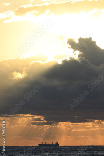 commercial cargo ship sailing in the sun and dark clouds