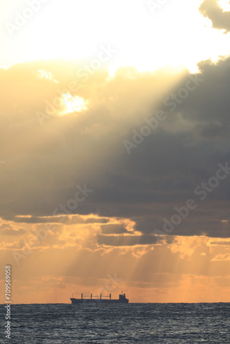 commercial cargo ship sailing in the sun and dark clouds