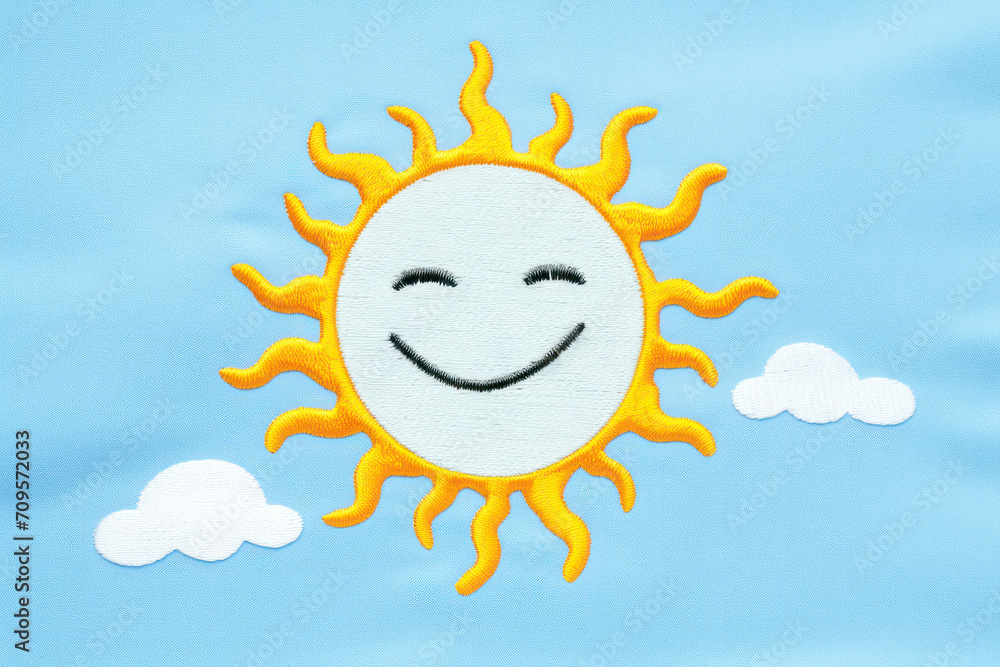 A basic embroidery depicting a small, smiling sun in chain stitch on a sky-blue fabric A basic embroidery depicting a small, smiling sun in chain stitch on a sky-blue fabric