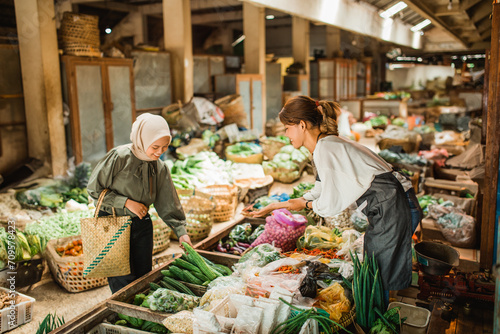 female customer picking vegetable from greengrocery stall in farmer market photo