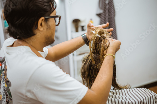 asian male hairstylist holding a comb and combing his customer hair