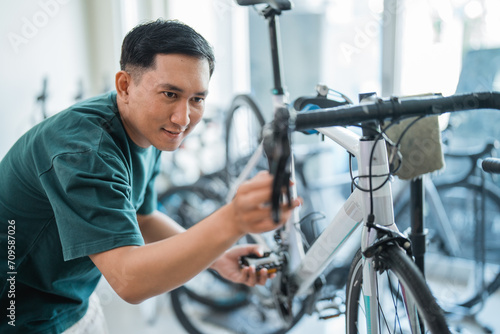 young Asian man seriously checks the pedals and handlebar of a new racing bike in a bike shop