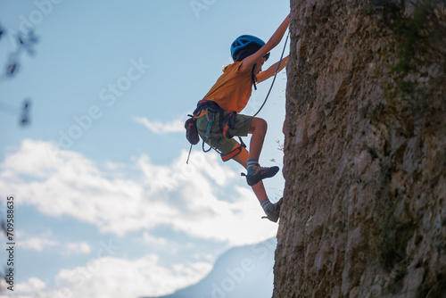 Obraz na płótnie A determined and strong boy climber climbs a steep mountain wall. Extreme sports and rock climbing. w salonie