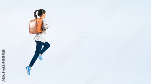 ランドセルを背負ってジャンプする女子小学生の後ろ姿（切り抜き背景透過PNGも販売しております。作成者リンクから「PNG」で検索してください） photo