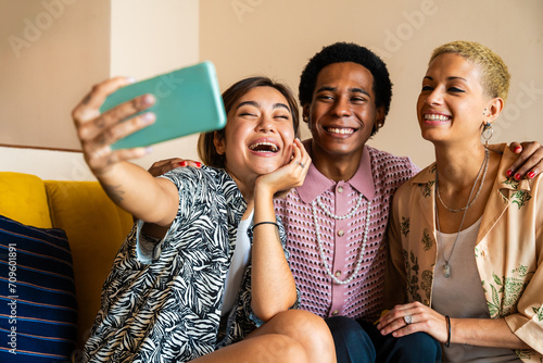 Group of friends bonding at home, LGBTQ and diversity concepts - Homosexual couple and fluid gender non binary young man with LGBT cross dressing clothing style having fun in the apartment photo