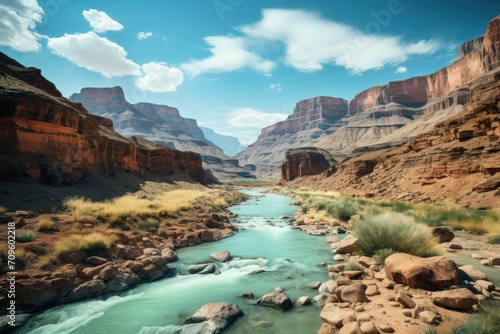  a river running through a canyon next to a rocky cliff covered in green grass and rocks and a blue sky with white clouds.