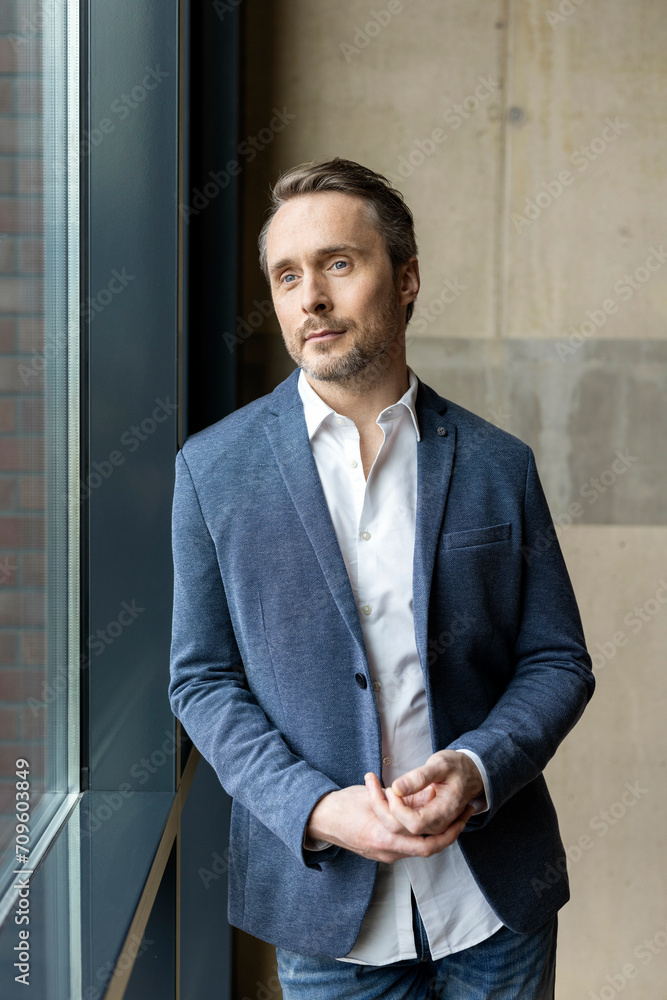 Contemplative mature businessman standing by window at office Contemplative mature businessman standing by window at office
