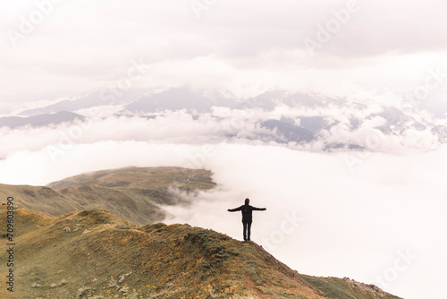Woman with arms outstretched standing on Mestia mountain near clouds photo