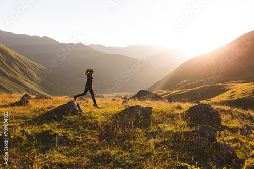 Woman jumping on rocks in front of mountains at sunset