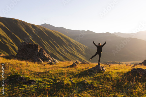Carefree woman with arms raised standing on rock in front of mountains at sunset photo